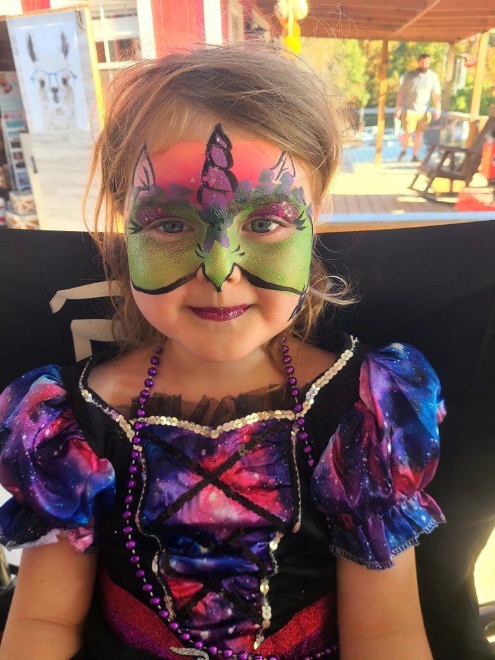 Glittery green and pink unicorn face paint on a young girl