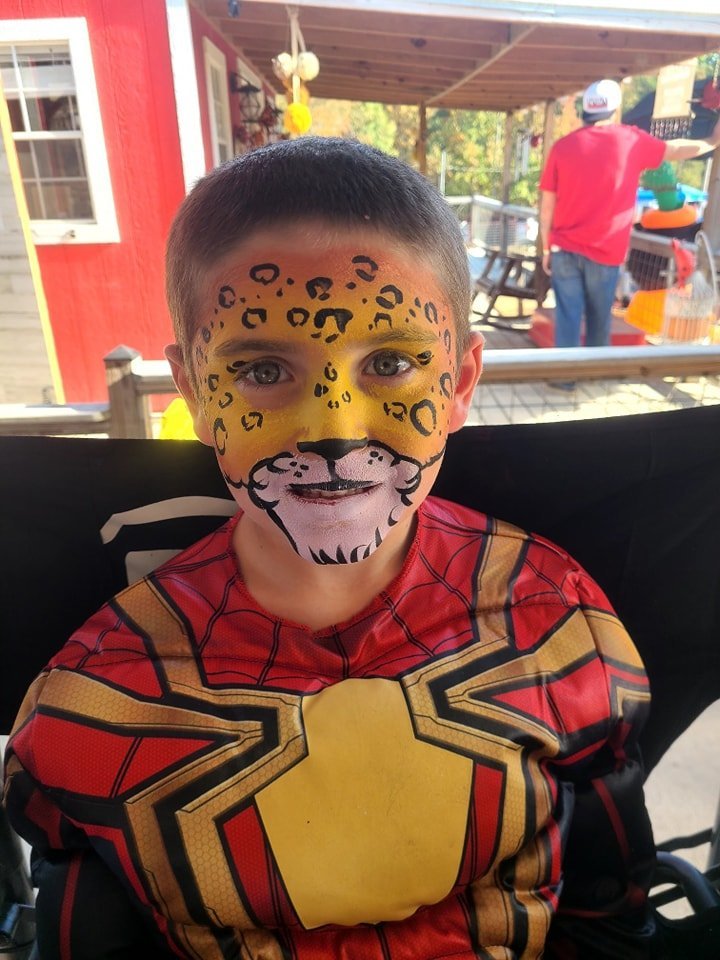 Detailed tiger face paint on a young boy in a Spider-Man shirt